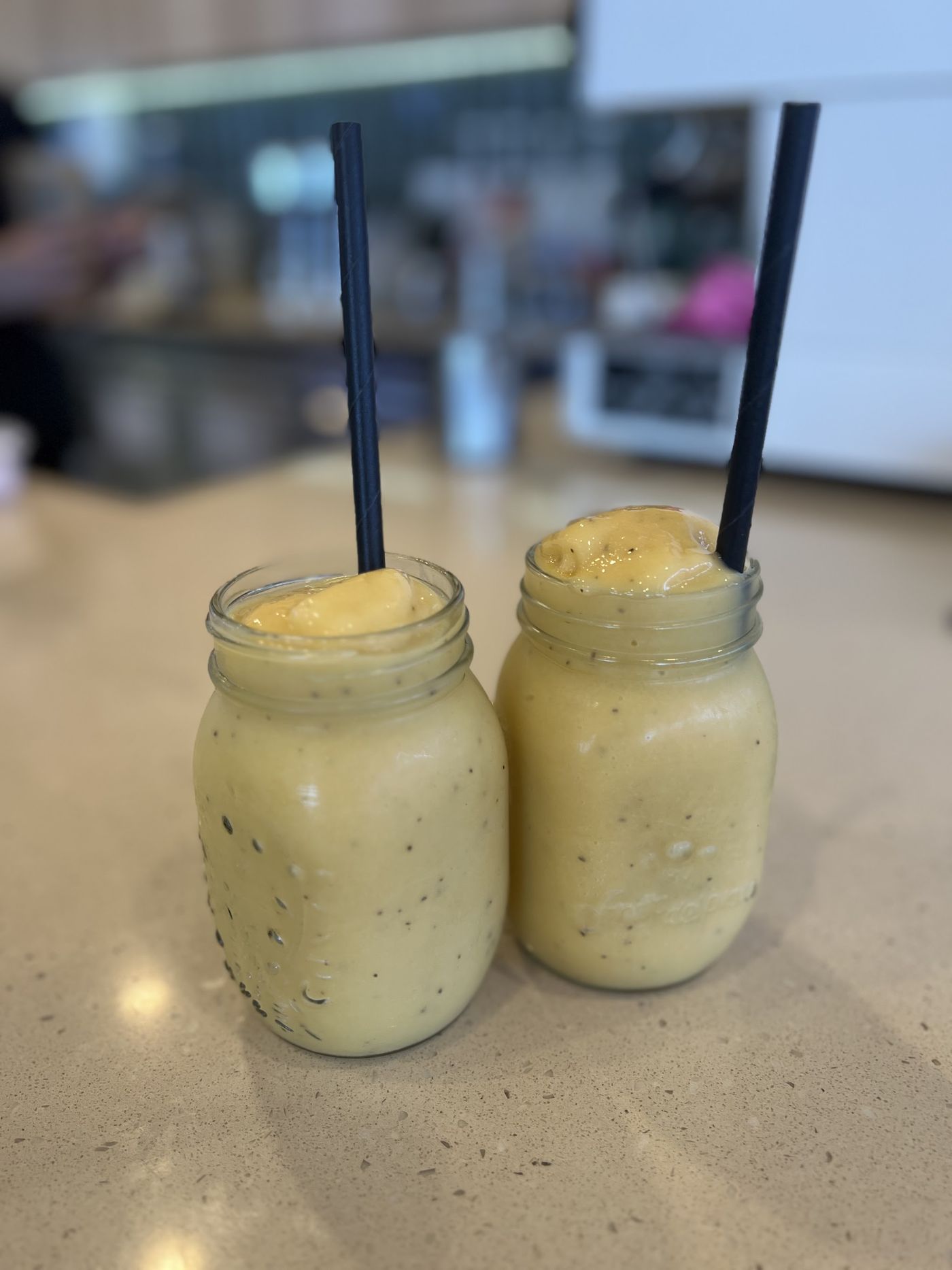 Two mango smoothies in mason jars on the AM Cafe counter
