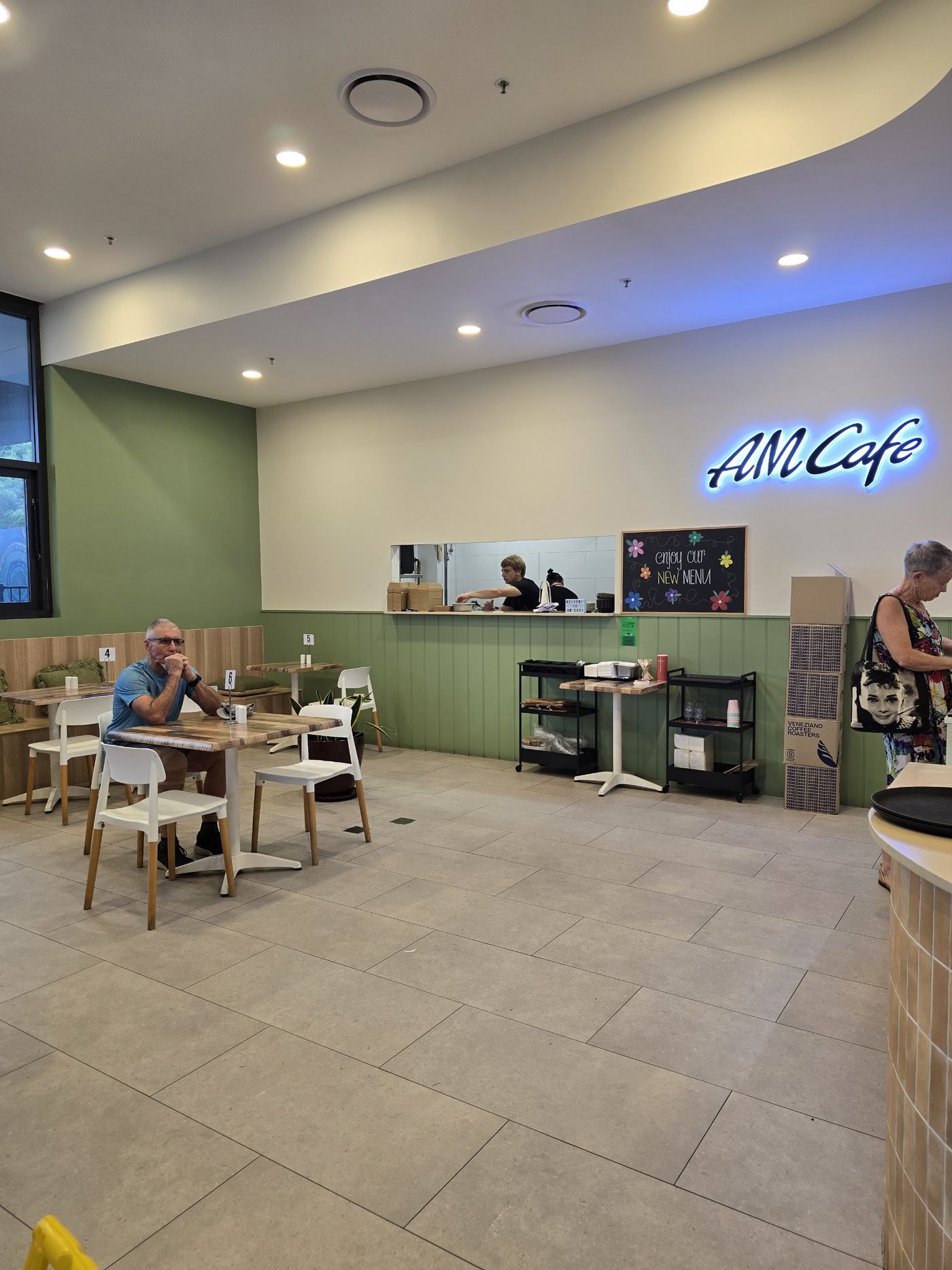 Inside AM Cafe, with sage green wainscoting and the lit AM Cafe sign